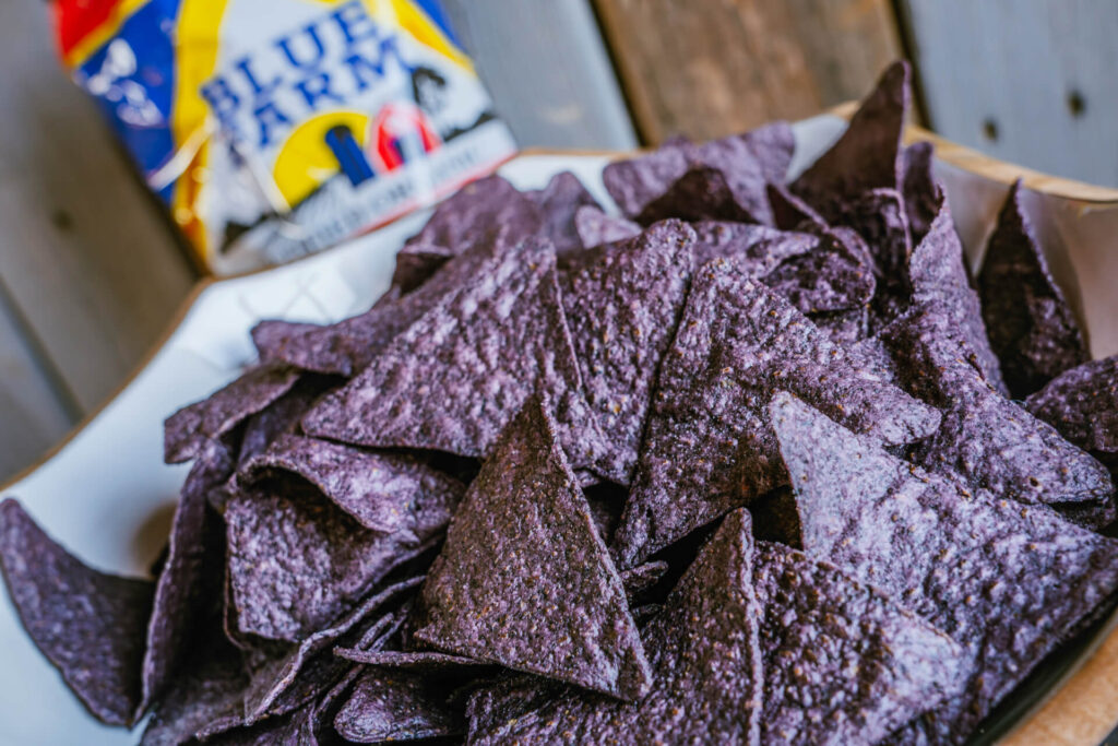 A closeup of a bowl of Blue Farm Organic Tortilla Chips with a bag of chips in the background